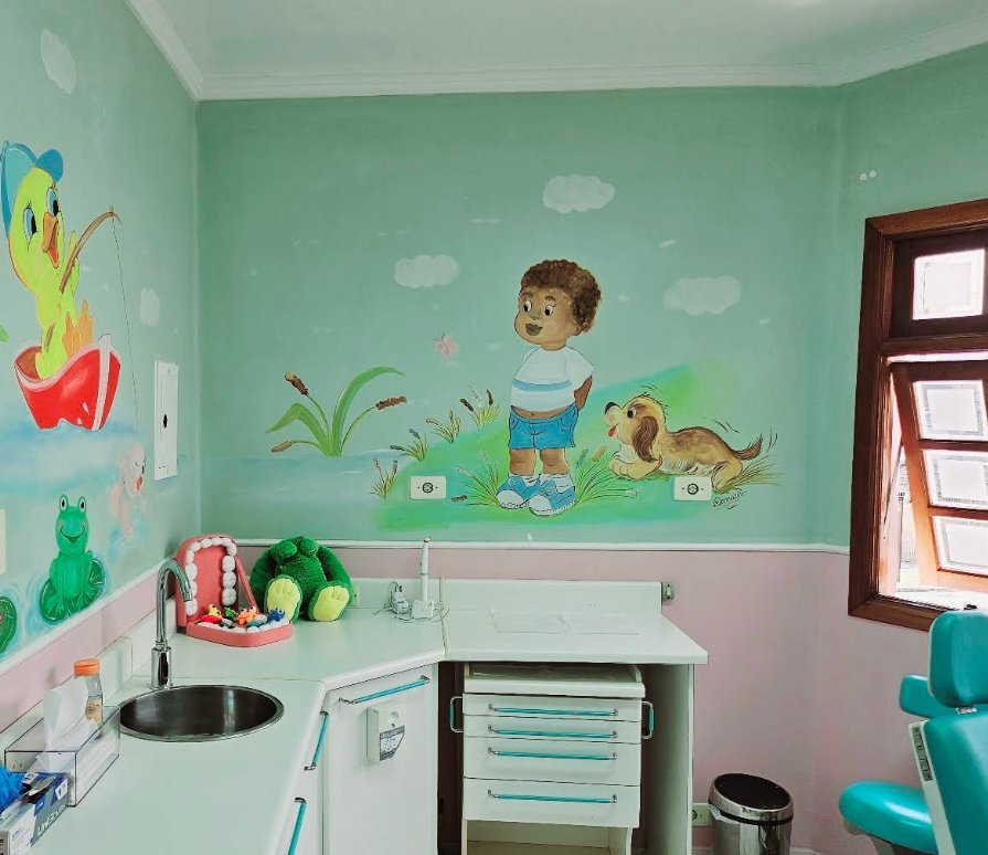 Sala de atendimento com mural pintado à mão, cadeira odontológica turquesa e bancada com brinquedos.